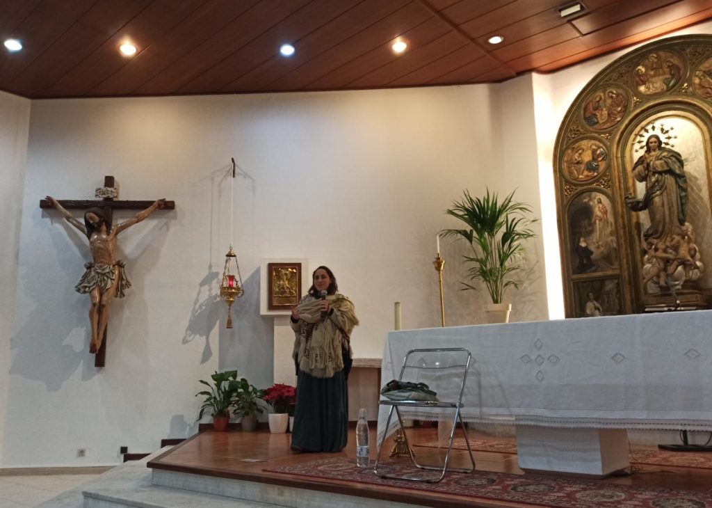María del Himalaya habla por un micrófono. junto al altar de la parroquia de Nuestra Señora del Rosario en Ibiza, con un gran crucifijo al fondo.